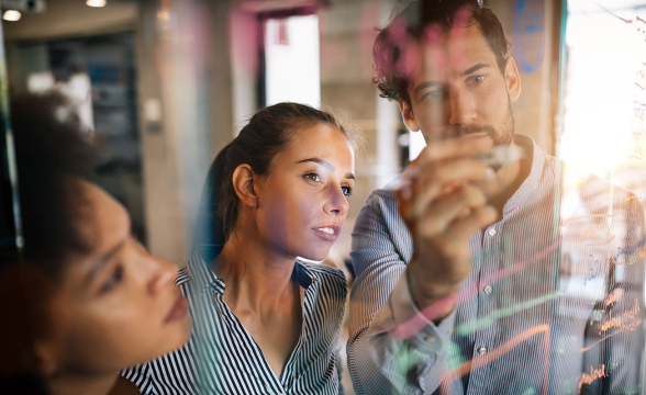 Zwei Frauen und ein Mann diskutieren vor einer Glaswand.