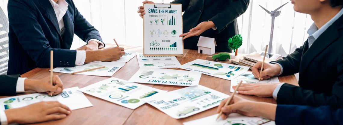 Mehrere Personen sitzen am Tisch und sprechen zu Unterlagen.