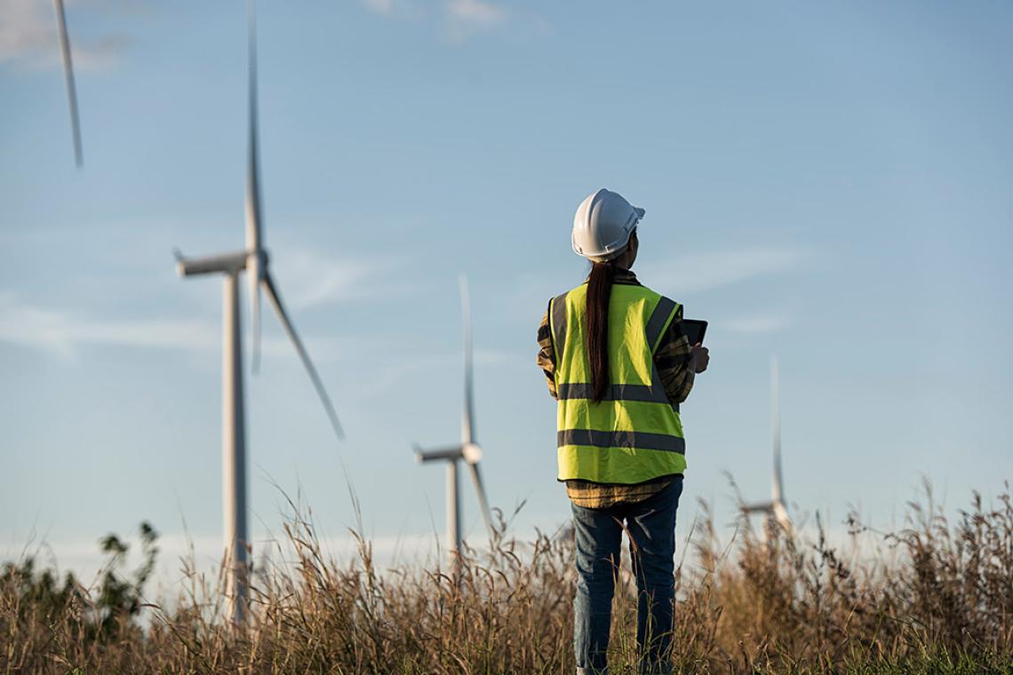 Frau mit Bauhelm steht in einem Feld mit Windrädern