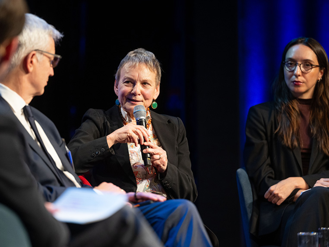 Eine Frau diskutiert auf einer Bühne mit weiteren Menschen.