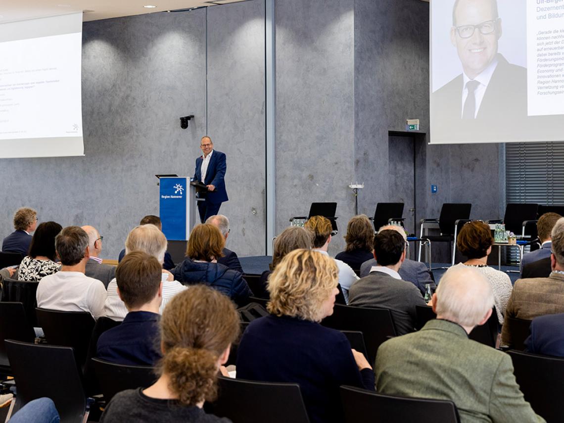 Ein Mann redet vor einer sitzenden Menschenmenge in einem Saal