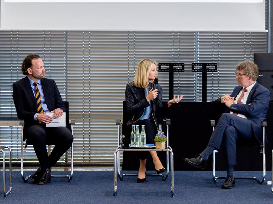 Eine Frau und zwei Männer sprechen vor einer Menschenmenge