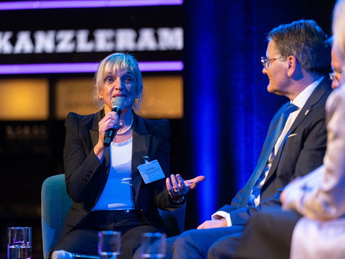 Eine Frau diskutiert auf einer Bühne mit weiteren Menschen.