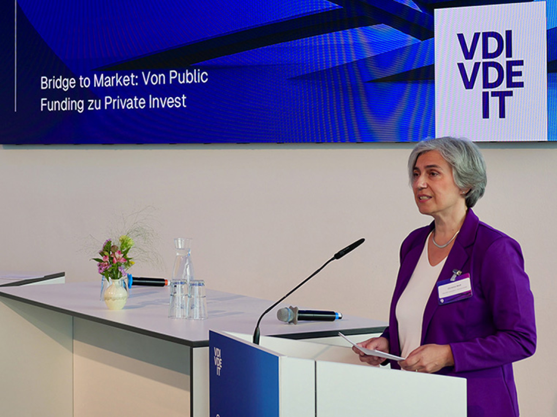 Eine Frau steht an einem Redepult und spricht in ein Mikrofon.