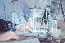 Hände auf einer Laptop-Tastatur. Im Vordergrund ist das Hologramm einer Stadt zu sehen.