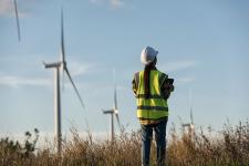 Frau mit Bauhelm steht in einem Feld mit Windrädern